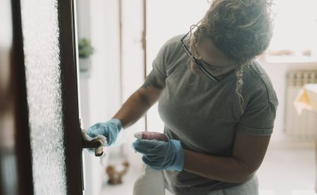 Domestic work at home. One woman cleaning door in apartment with spray and gloves. Housewife